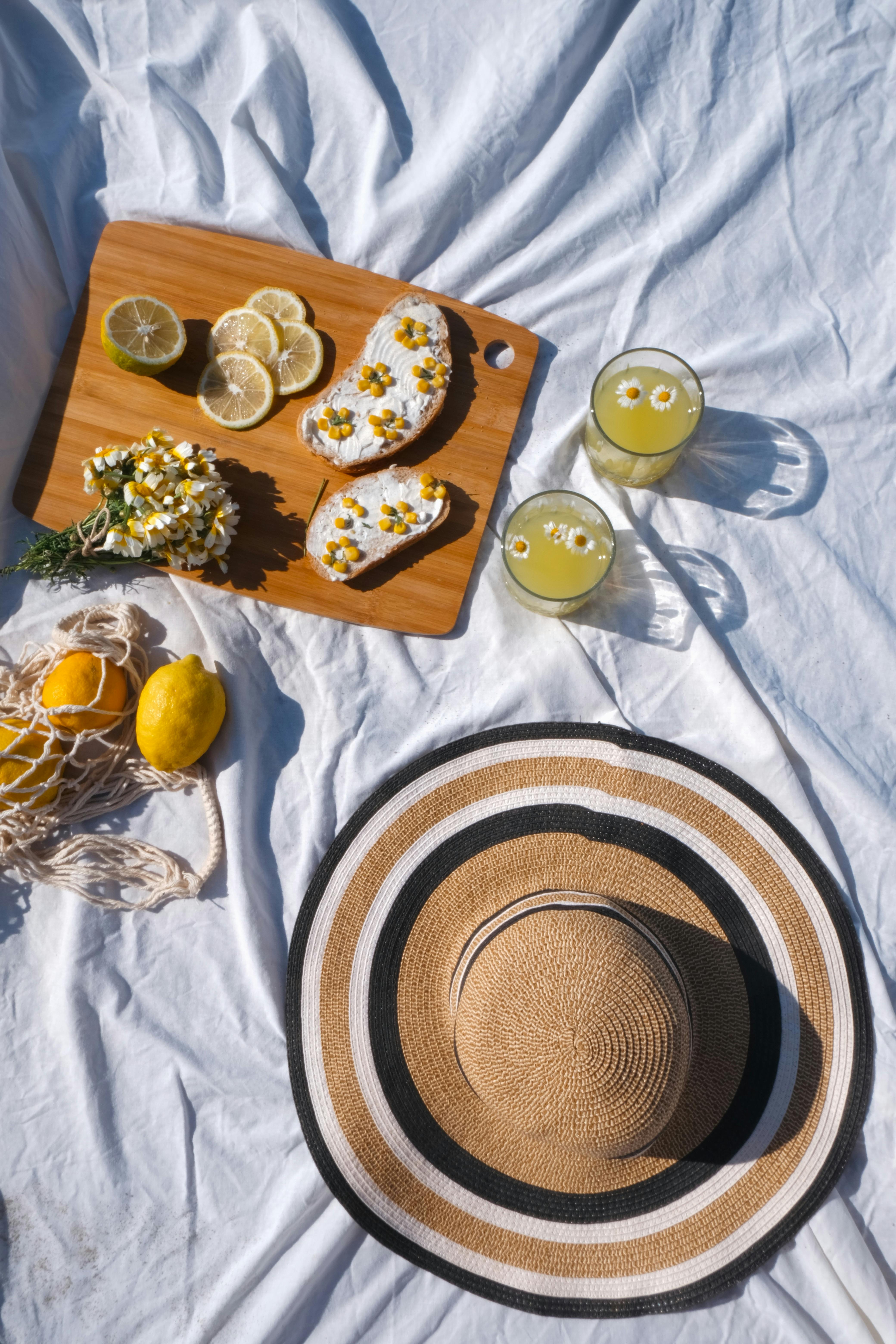 Top view of a summer picnic with lemonade, snacks, and a straw hat on a blanket.