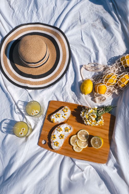 Free A bright outdoor picnic scene with lemons, sunhat, and floral embellishments on a wooden board. Stock Photo