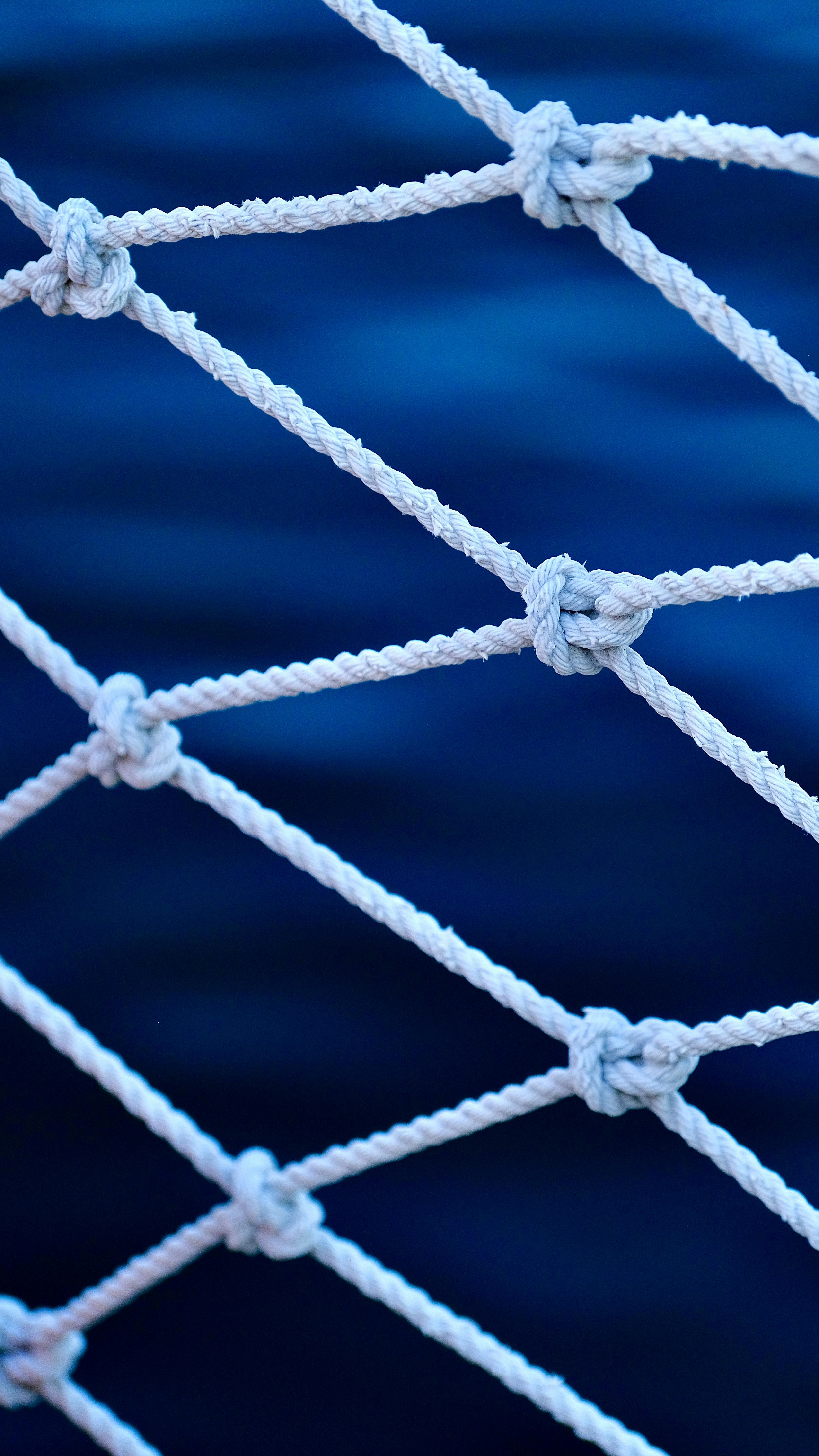 Detailed view of a fishing net with knots against a blurred blue sea background.