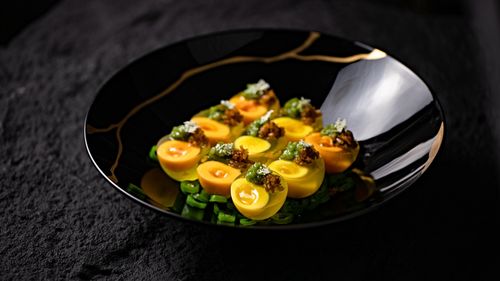 Free Delicious gourmet dish featuring artistically plated eggs with fresh greens on a decorative black plate. Stock Photo
