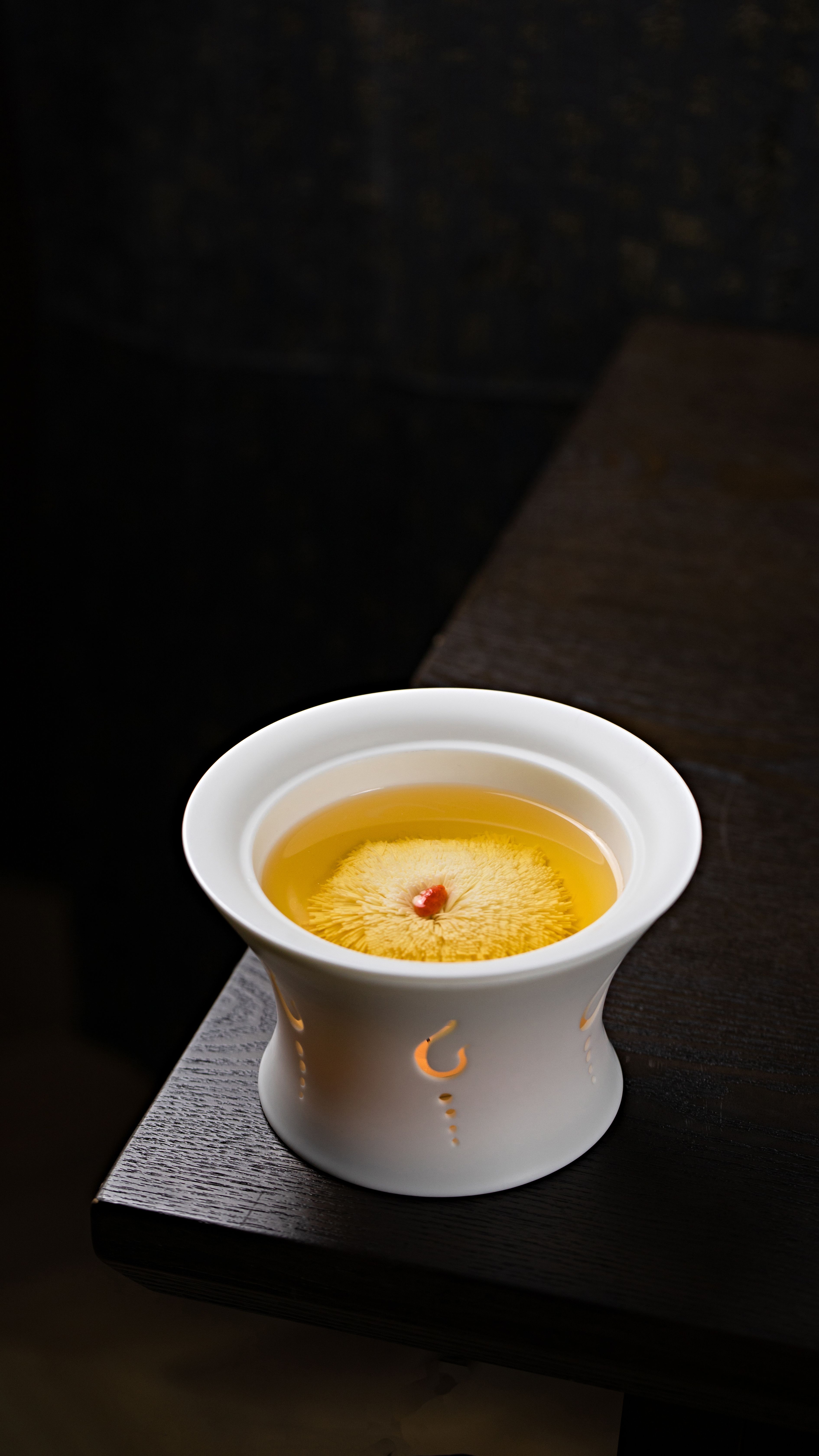 A stylish white ceramic cup holding warm chrysanthemum tea with a floral infusion on a dark background.