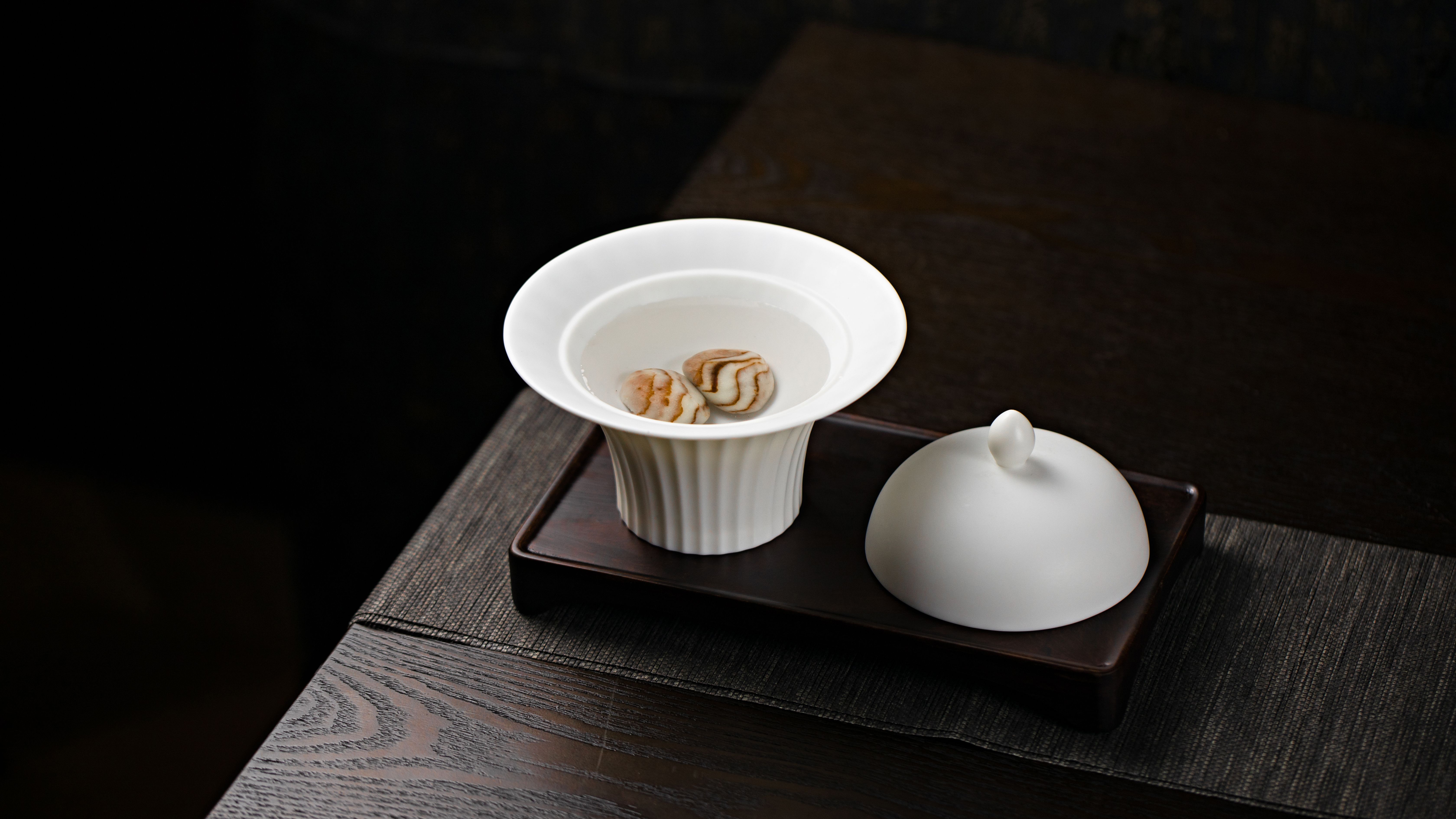A close-up of a white porcelain tea set on a dark wood tray with a black background.