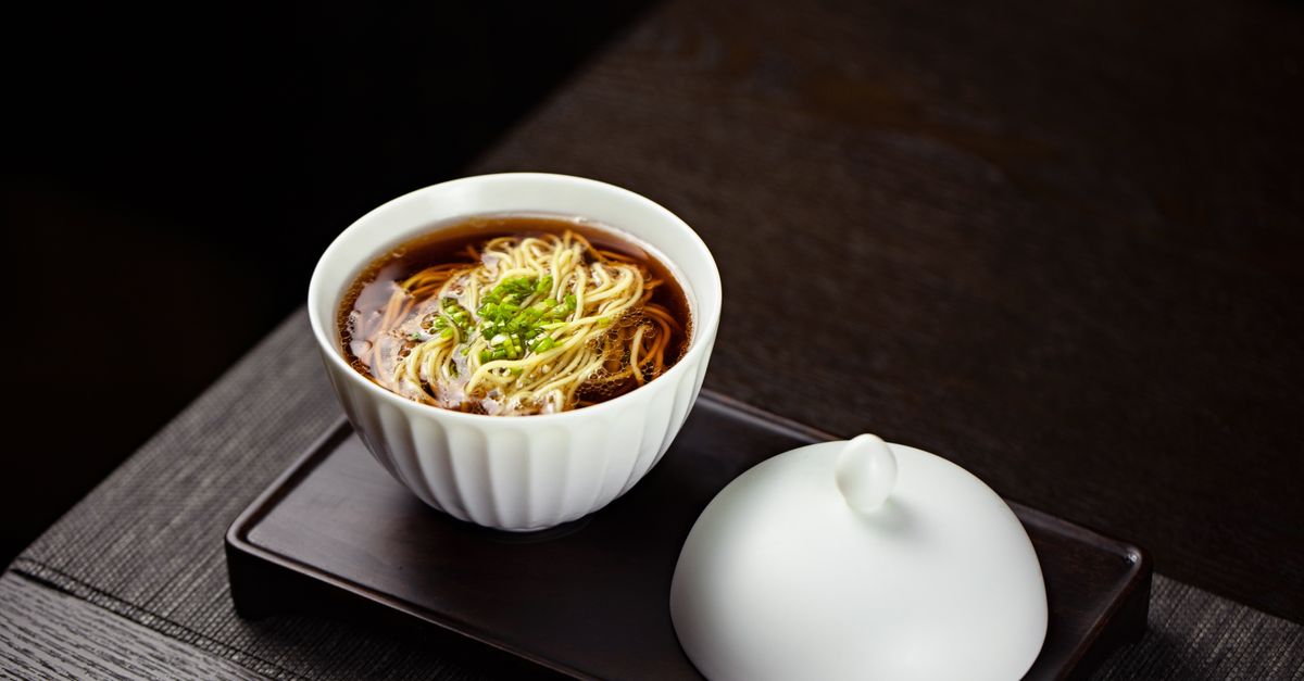 A close-up of a tasteful noodle soup garnished with greens, served in a bowl.