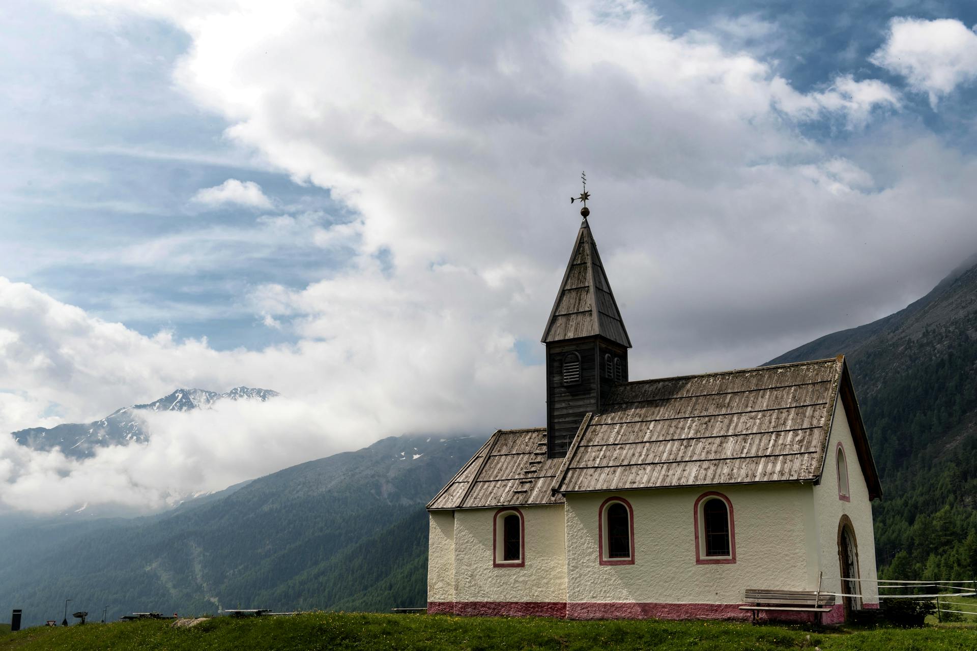 Peaceful church in Meran, Italy, set against scenic mountain backdrop with clouds.