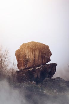 雾气缭绕的户外景观中，一名孤独的徒步旅行者站在巨大的岩石旁
