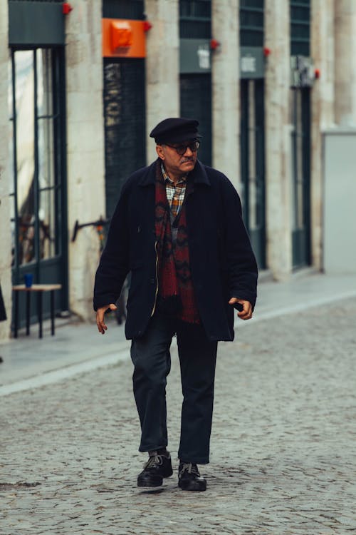 A man in a hat and coat walking down a street