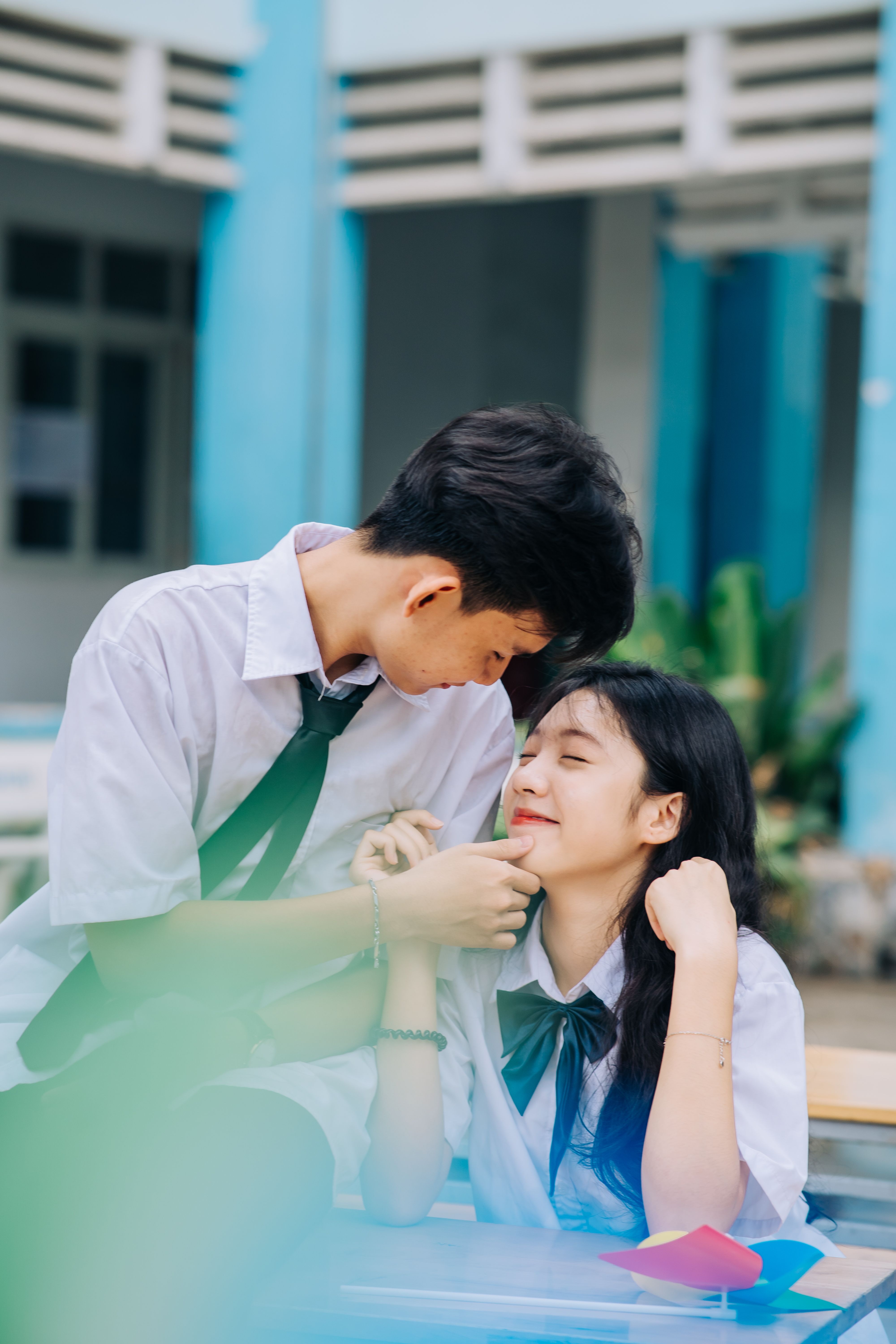 Playful and happy Asian teenage couple smiling while interacting outside school in uniforms.