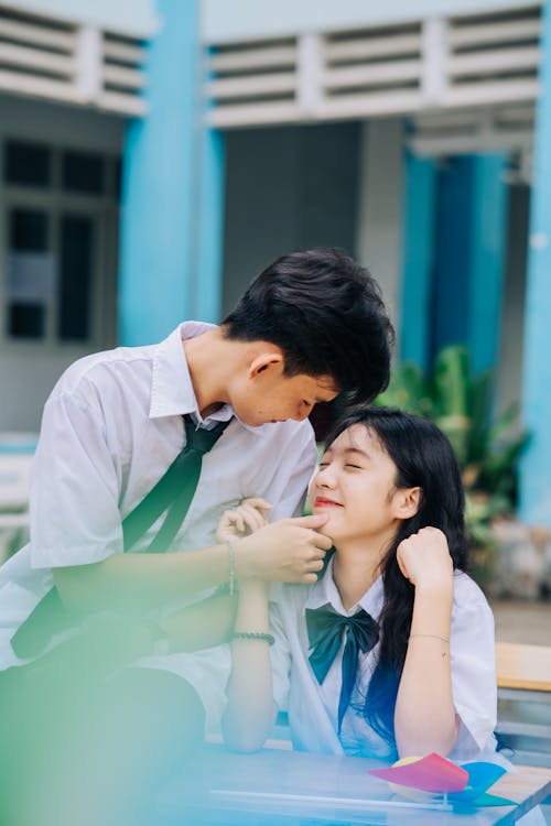 A young couple sitting on a bench in front of a school