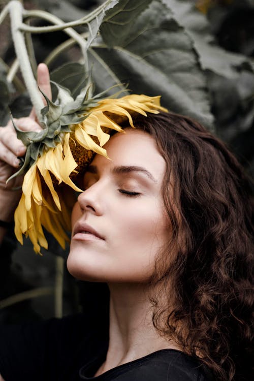 Side View Portrait Photo of Woman With Her Eyes Closed Posing With Yellow Sunflower Against Face