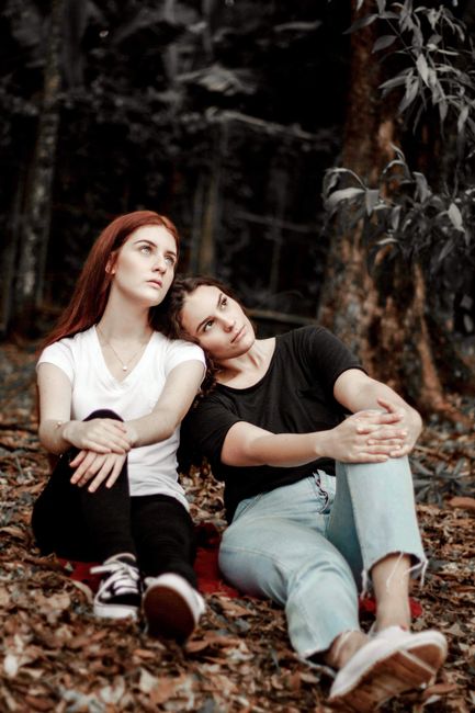 Two women sitting on leaves in a serene forest, enjoying leisure time.