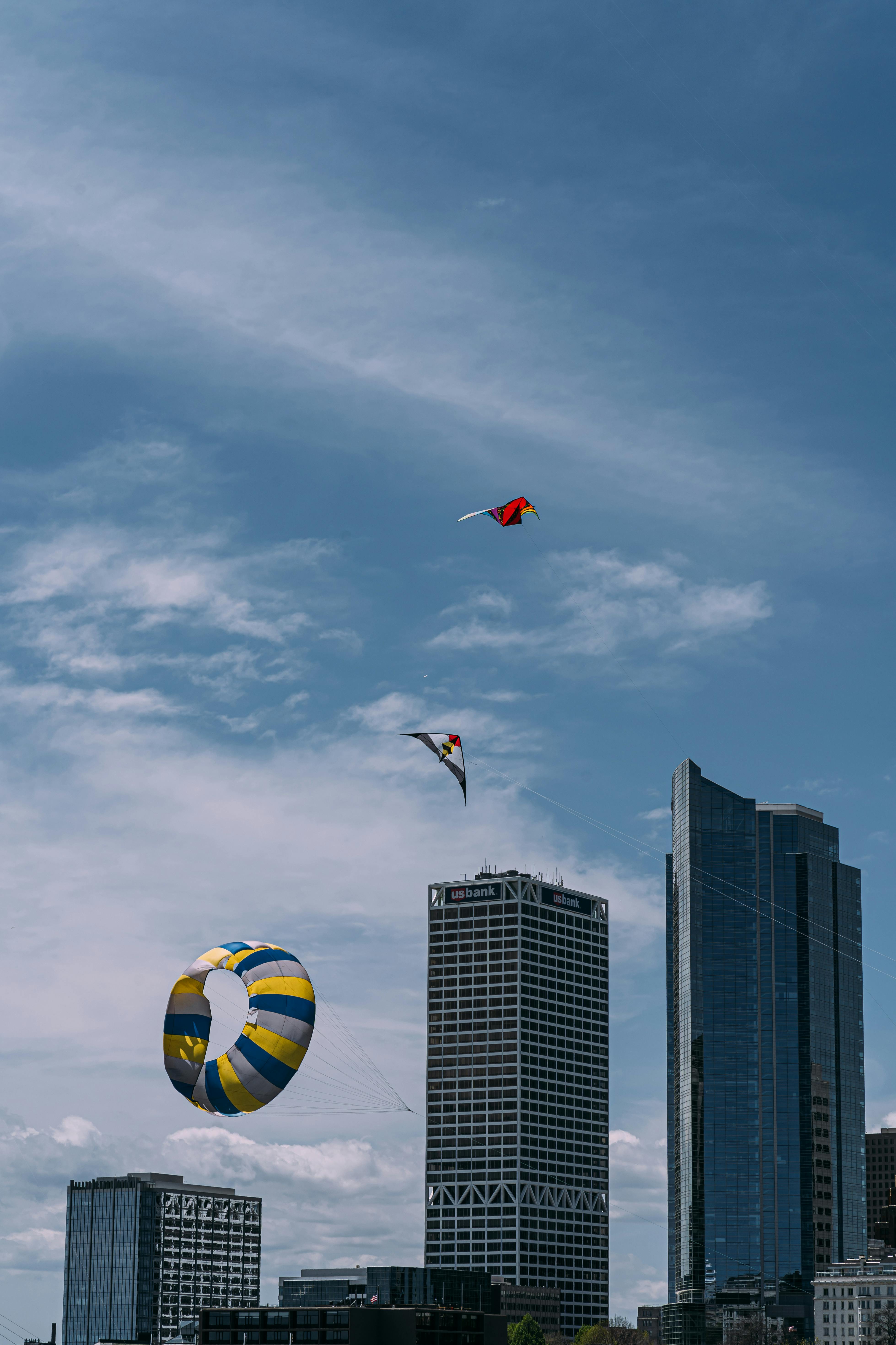 Colorful kites flying over urban skyscrapers against a clear blue sky.