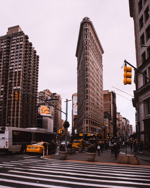 Free Vibrant street scene of New York's Flatiron Building with bustling traffic and city life. Stock Photo