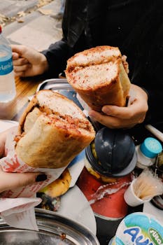 Two sandwiches held close-up, showcasing a delicious café setting with hands and table view.