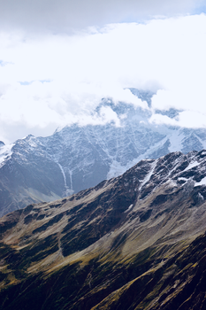 Spectacular view of a snow-capped mountain range enveloped by clouds under a bright sky.