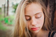 一位长着雀斑的少女在户外树旁向下看的特写肖像