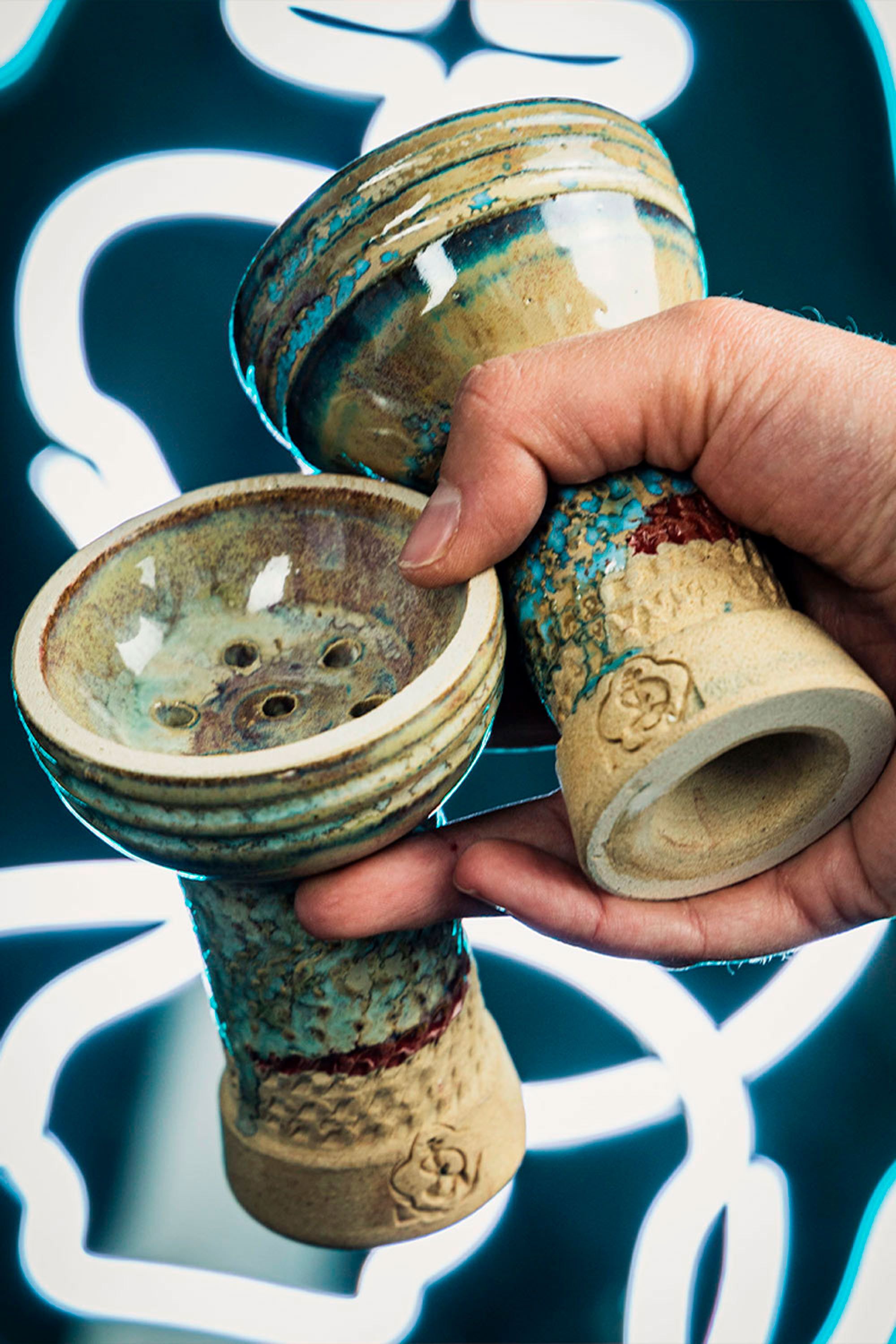 Close-up of a hand holding two artisan ceramic phunnel bowls against a blurred background.