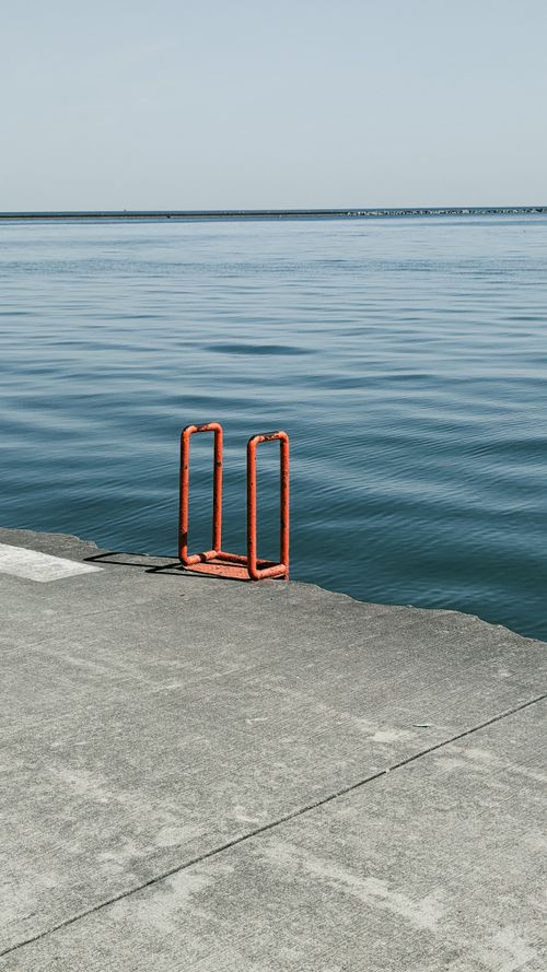 Free Peaceful seaside pier featuring a striking red ladder against a calm ocean backdrop. Stock Photo