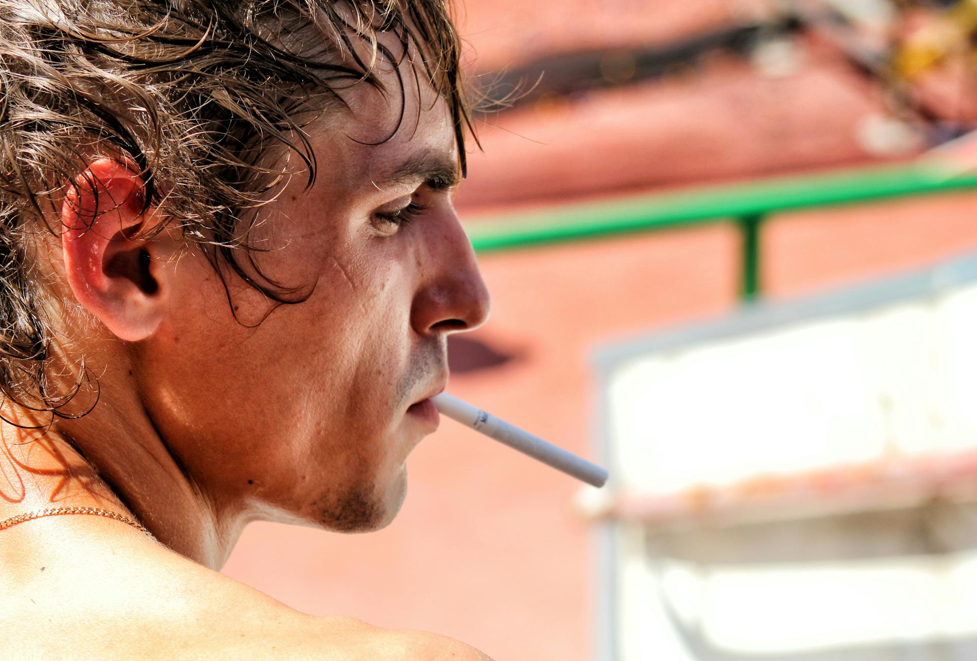 Close-up of a young man smoking a cigarette in an outdoor setting on a sunny day.