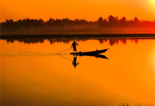 Silhouette of Man Standing on Boat in the Middle of the Lake