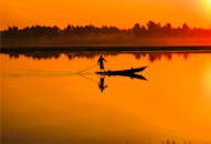 宁静的湖面上，日出时分，一名渔夫乘坐独木舟的剪影