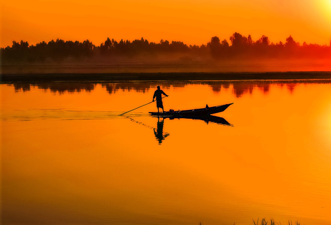 Free Silhouette of Man Standing on Boat in the Middle of the Lake Stock Photo