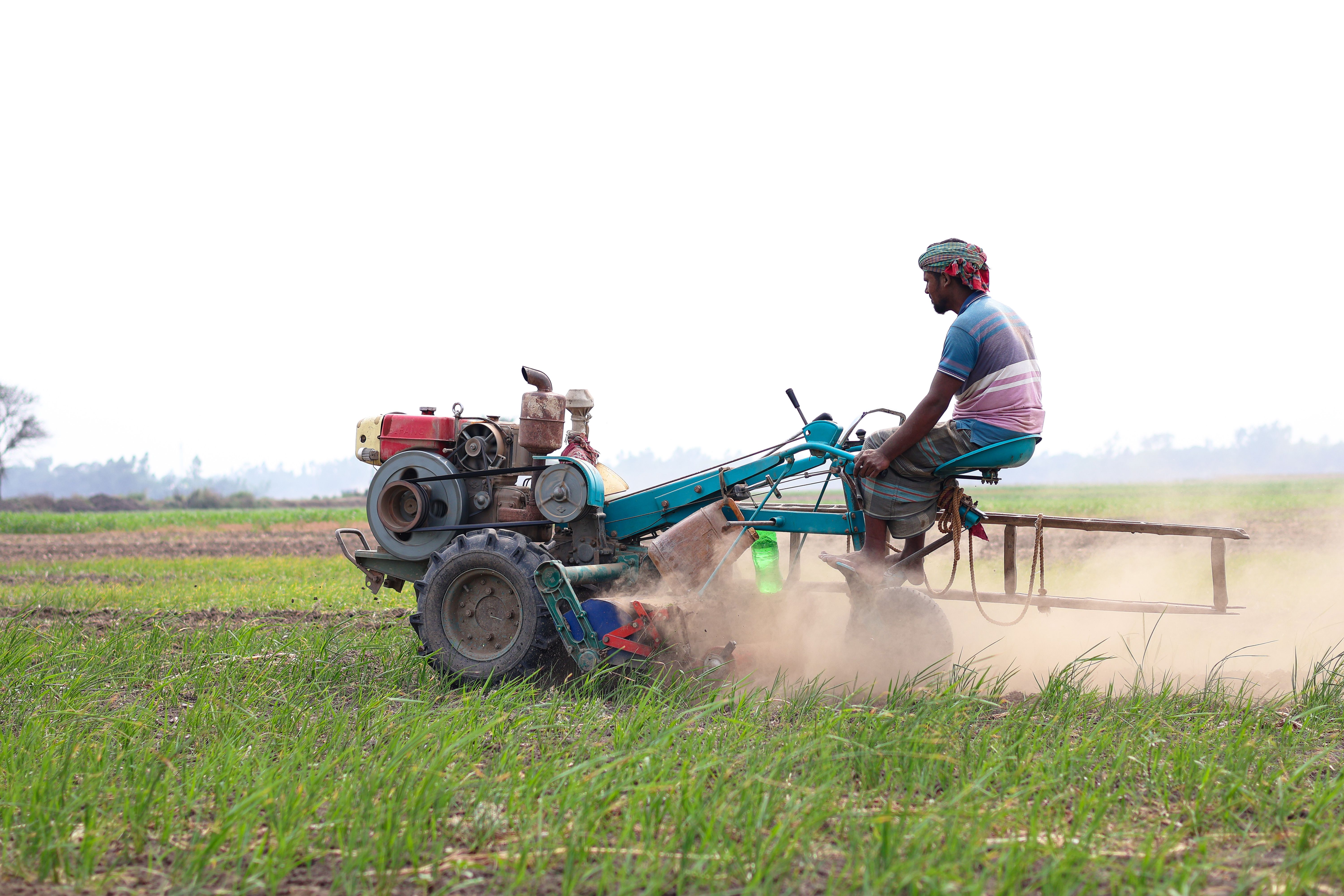 A farmer working a tractor in a green field during the day in Pabna, Bangladesh.