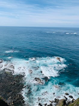 从空中俯瞰，海岸线岩石崎岖，海浪碧绿，天空湛蓝清澈