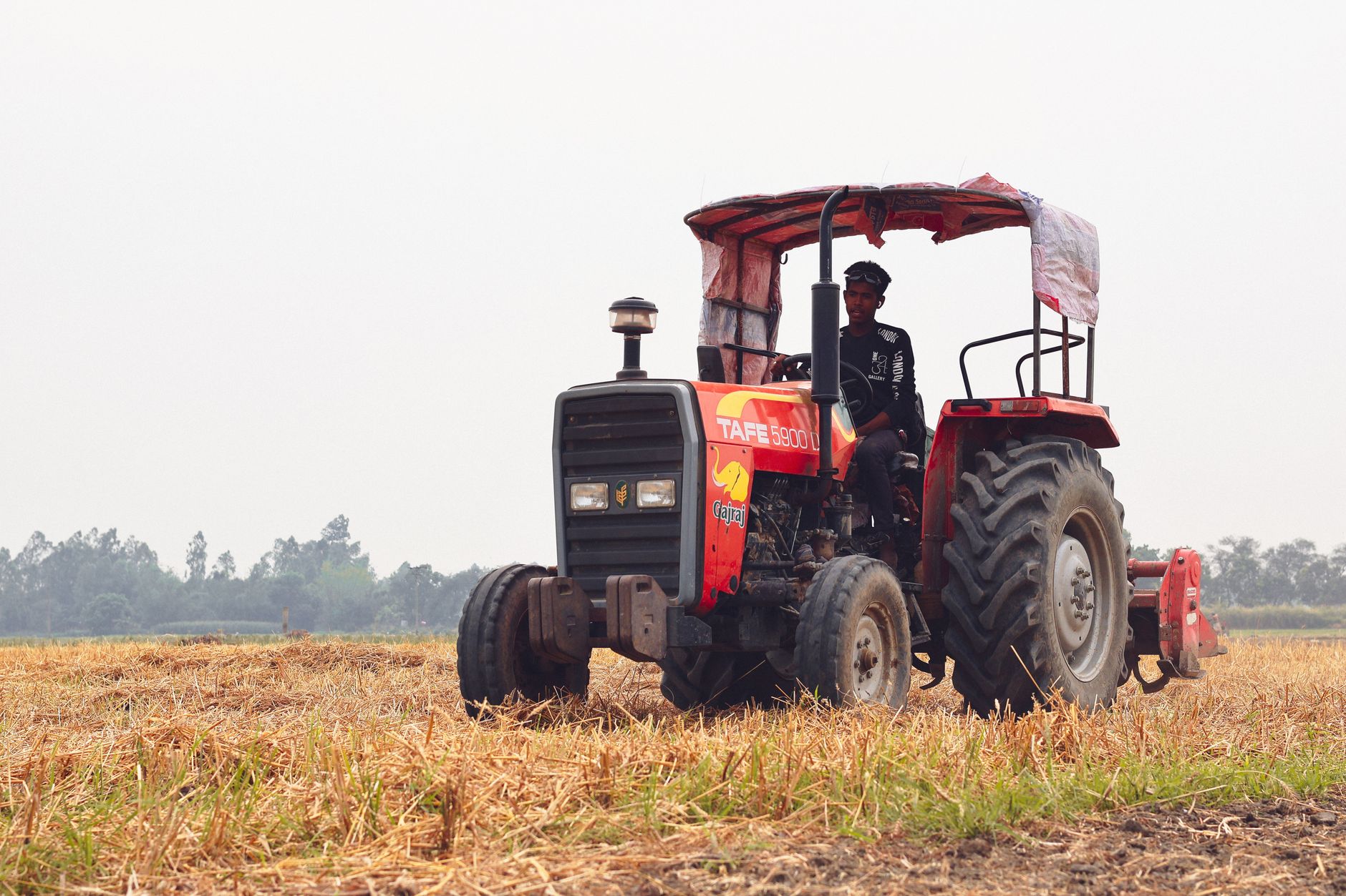 A farmer drives a red tractor across a harvested field in Pabna, Bangladesh.