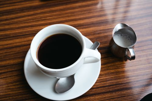 Free A warm coffee cup on a wooden table, accompanied by a metal milk jug. Cozy and inviting. Stock Photo
