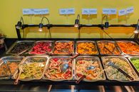 Colorful selection of Asian dishes displayed in a buffet with serving utensils.