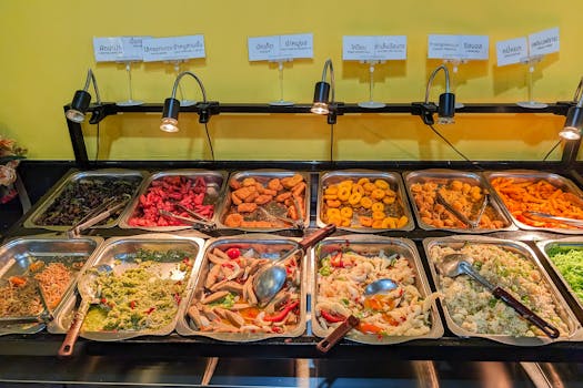 Colorful selection of Asian dishes displayed in a buffet with serving utensils.