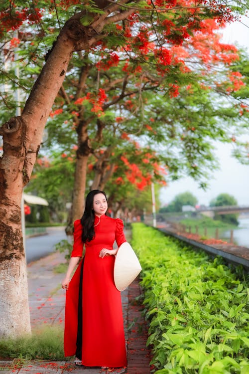 A woman in a red dress stands on a sidewalk