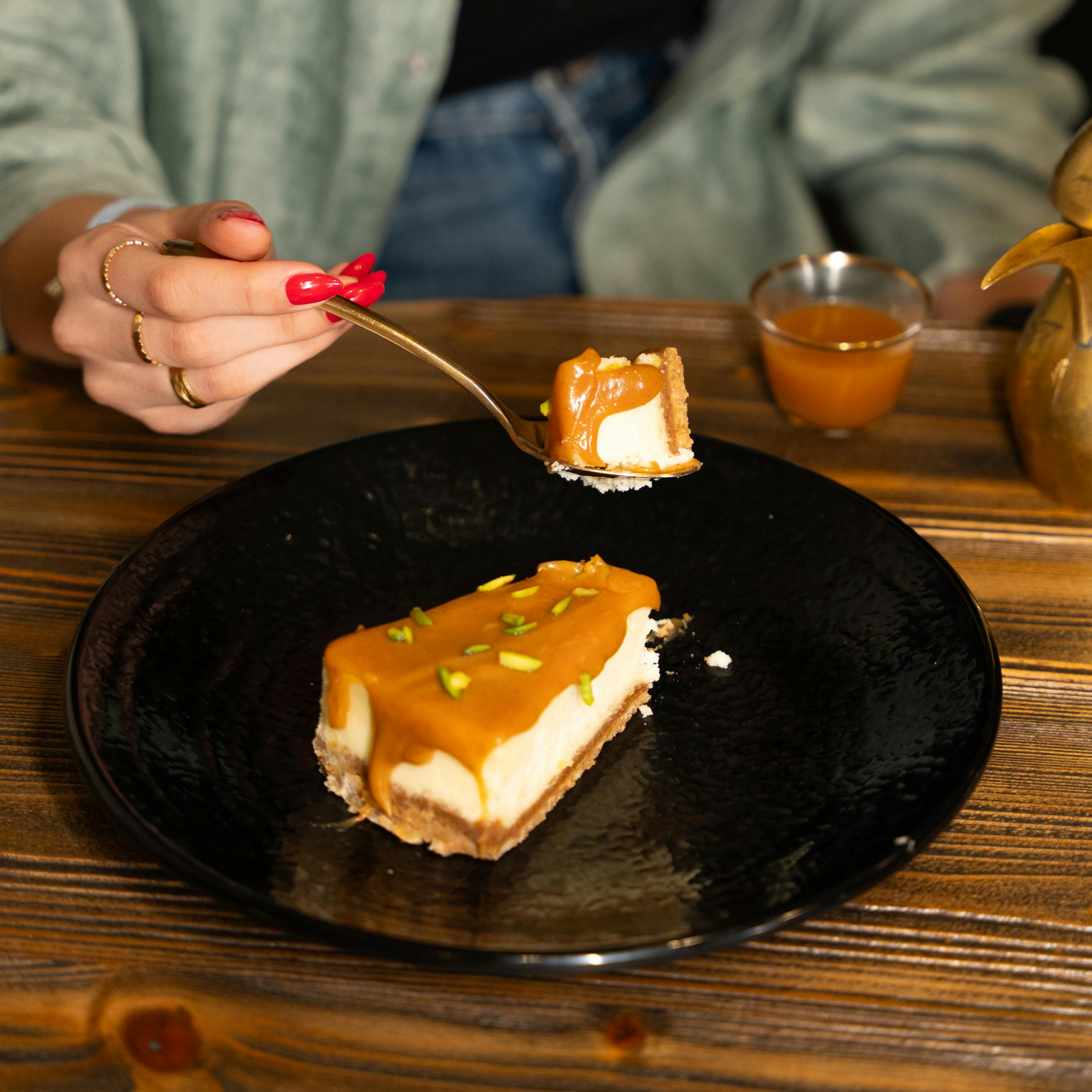 Indulge in a slice of caramel cheesecake topped with pistachios, served on a rustic table.