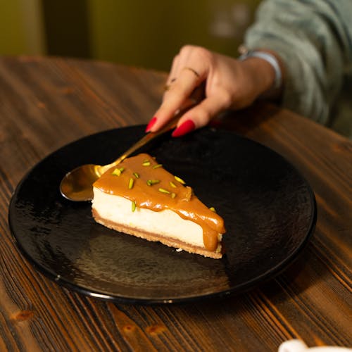 A person is holding a fork and knife over a slice of cheesecake