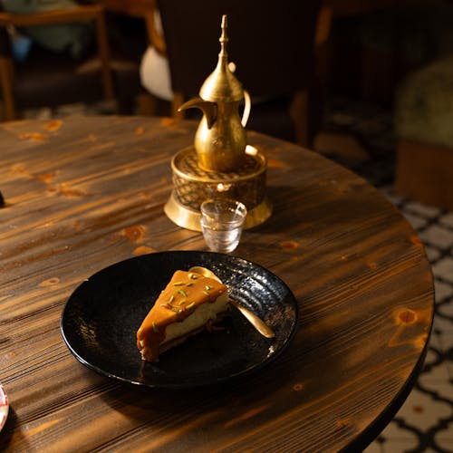 A slice of cake on a table next to a tea pot