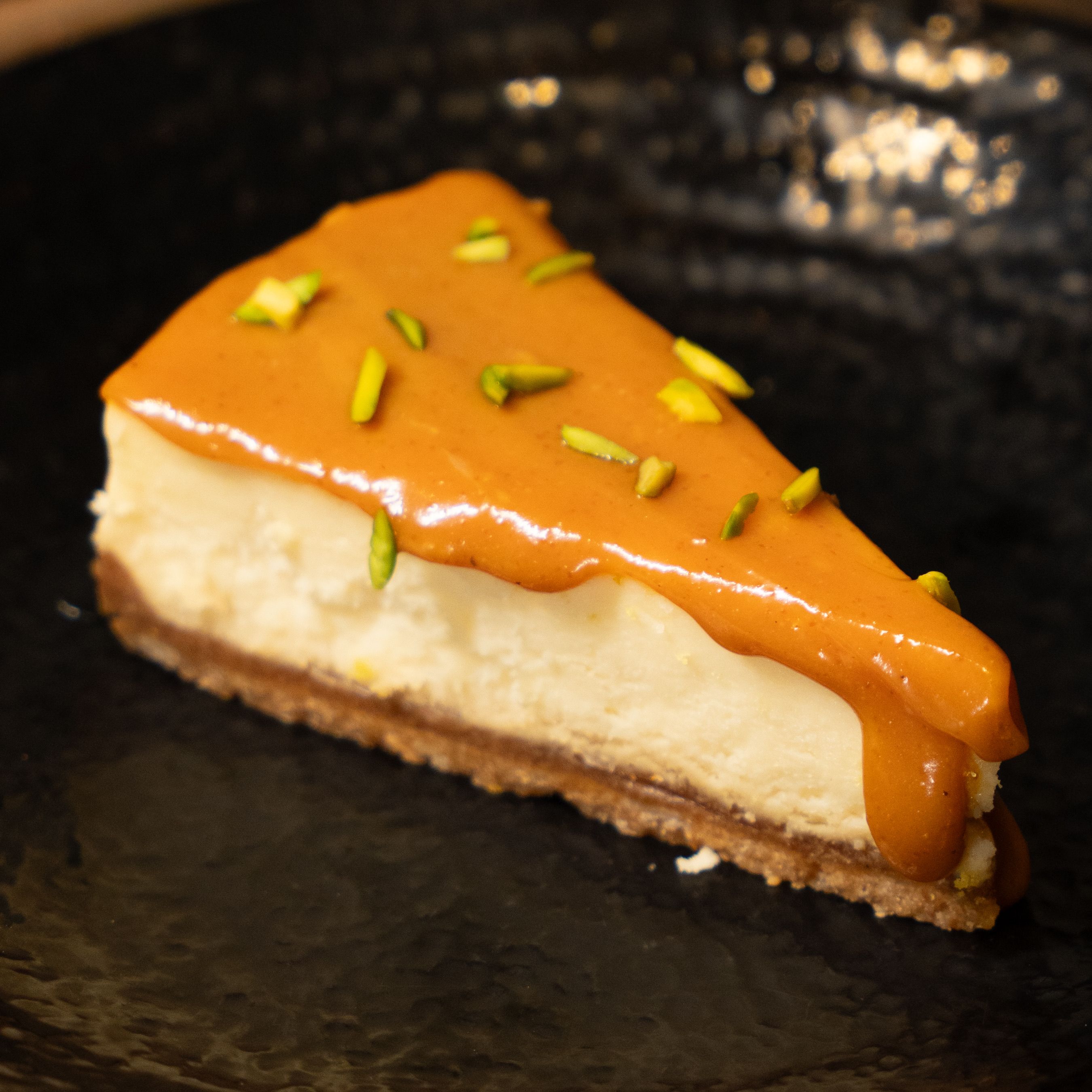 Close-up of a creamy cheesecake slice with caramel topping garnished with pistachios.