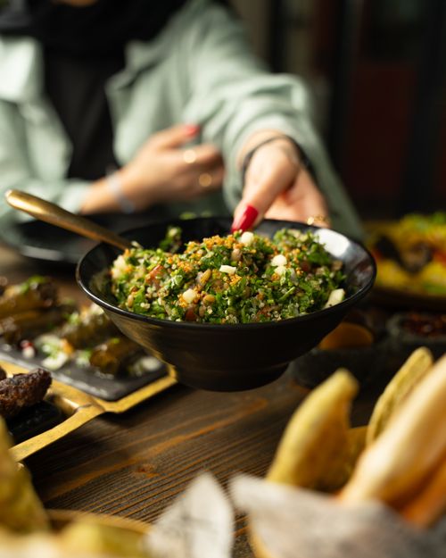 Free A hand reaches for a bowl of fresh tabbouleh salad on a rustic wooden table, perfect for food photography. Stock Photo