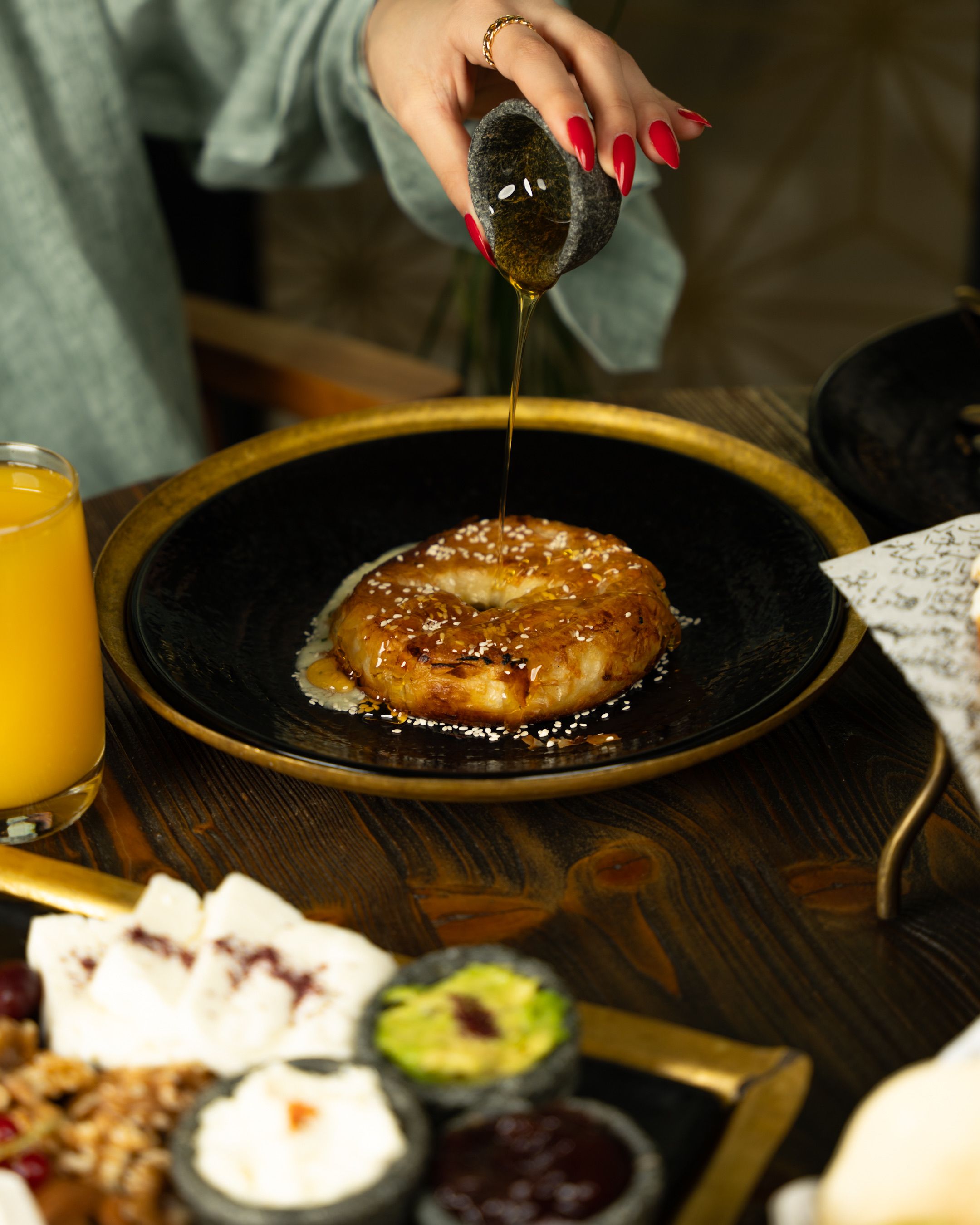 A mouthwatering bagel on a black plate being drizzled with honey, perfect for a cozy breakfast.