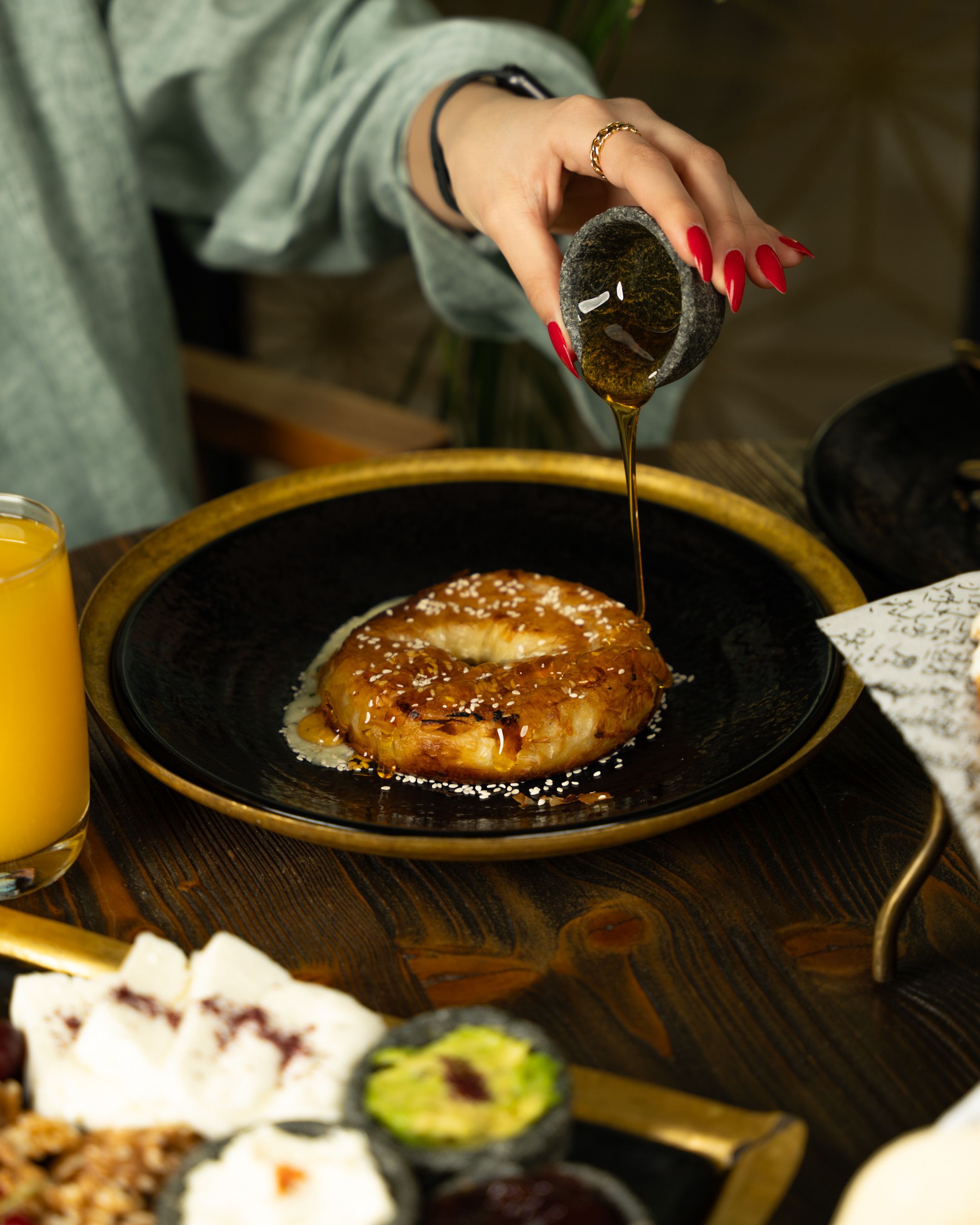A woman's hand pouring honey over a round pastry served on a black plate.