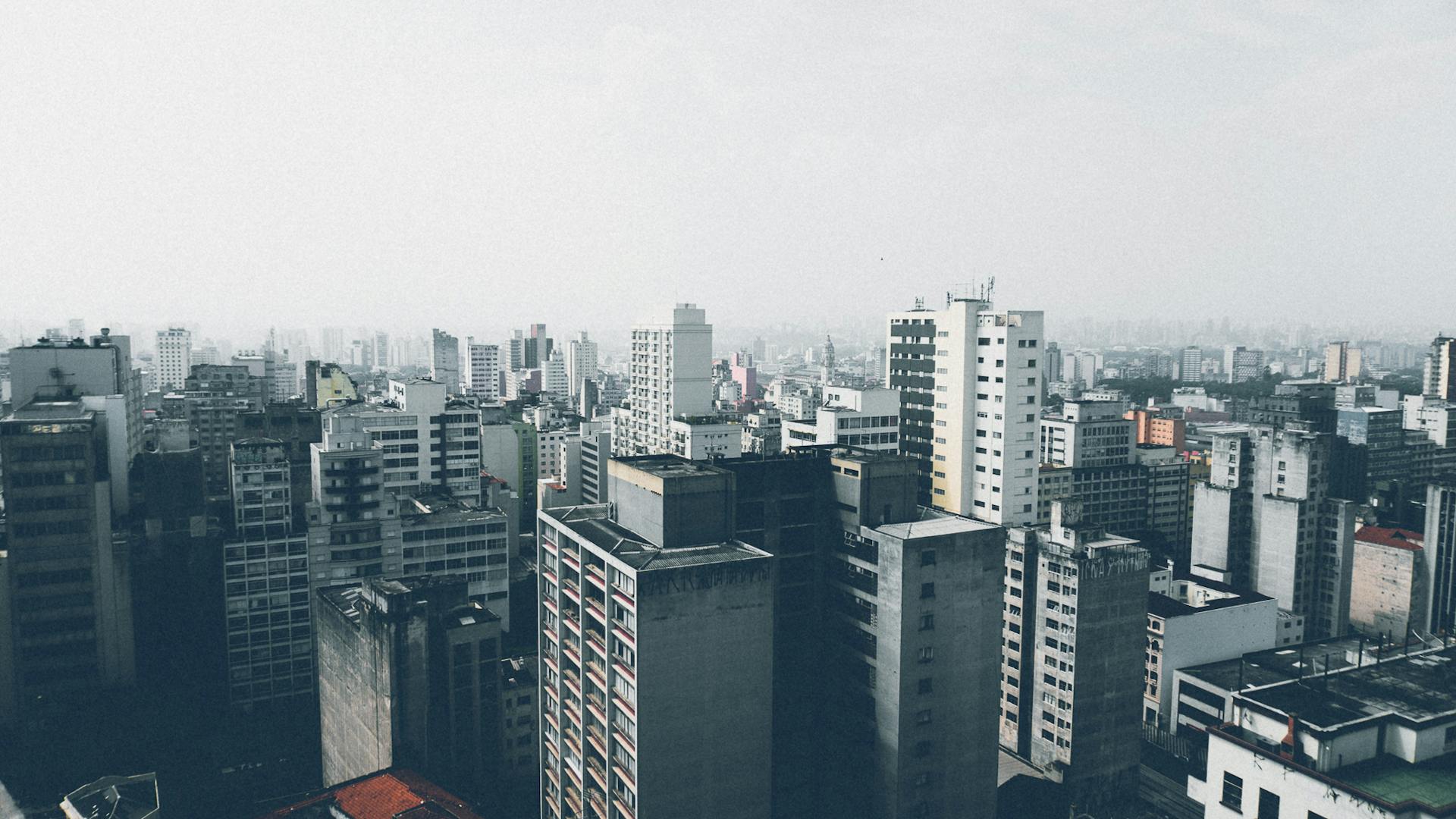 Aerial view of a dense urban cityscape with numerous skyscrapers and high-rise buildings under a cloudy sky.