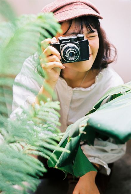 Smiling woman photographer taking a photo among lush greenery outdoors.