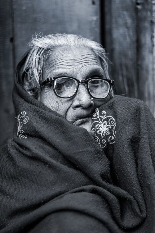 Free Close-up black and white portrait of an elderly woman with eyeglasses wrapped in a warm shawl. Stock Photo