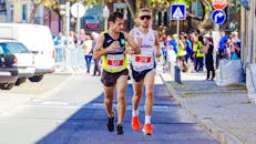 在一个阳光明媚的日子里，两名男性跑步者在城市马拉松比赛中激烈竞争