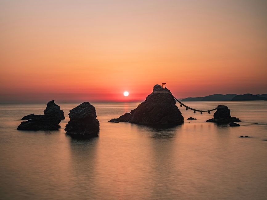 Serene ocean view at sunrise with dramatic rock formations and calming waters.
