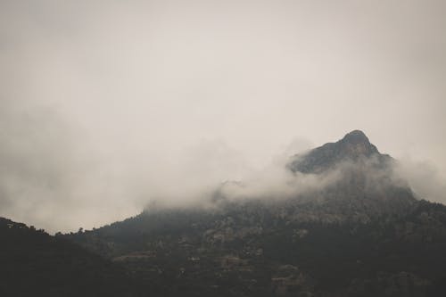 Free Breathtaking scenery of rough high mountain peak covered by fog on overcast day Stock Photo