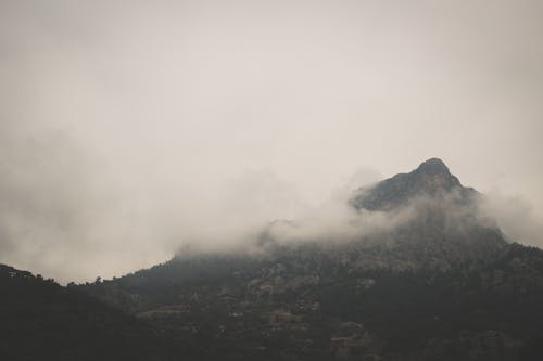 Breathtaking scenery of rough high mountain peak covered by fog on overcast day