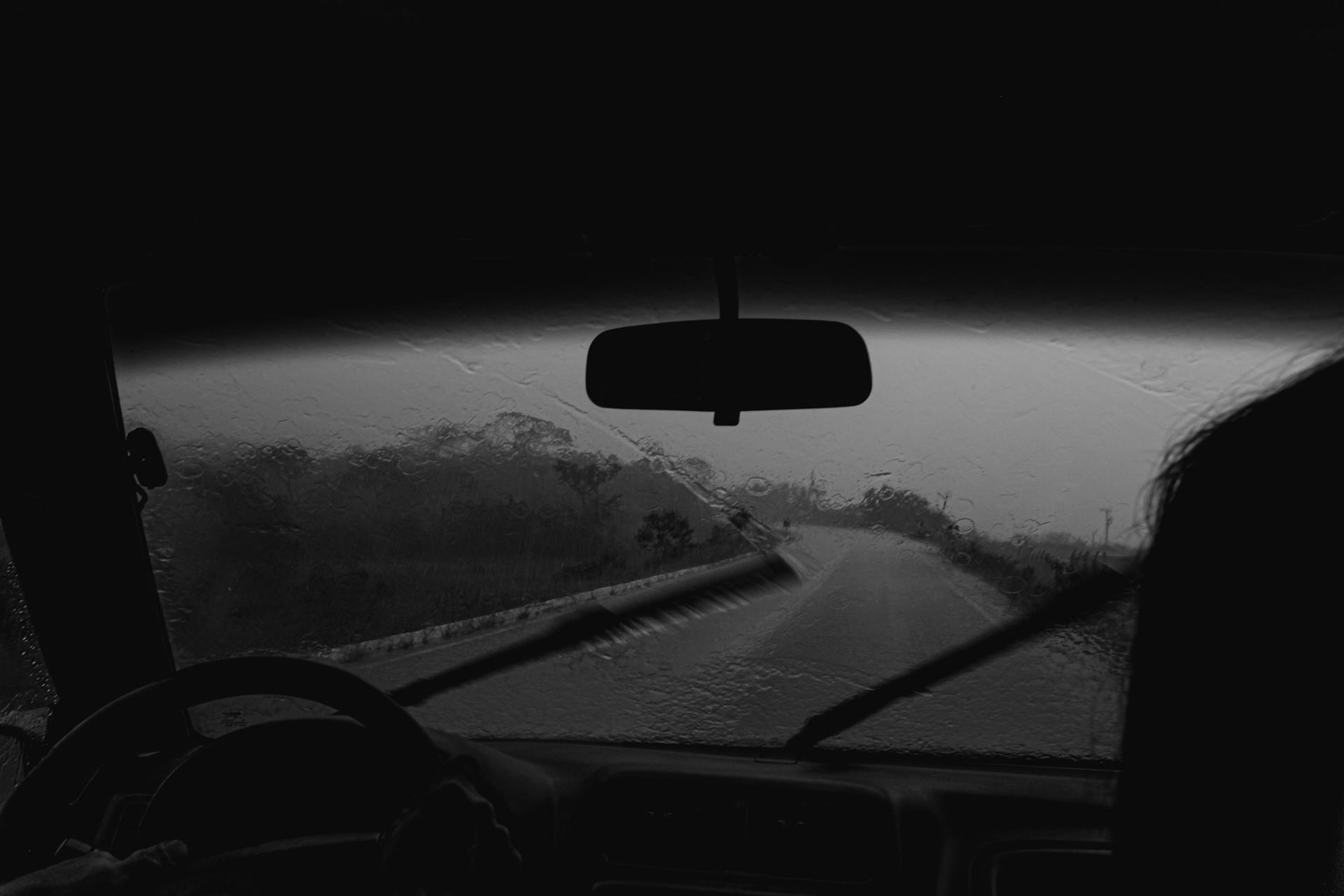 View from a car interior during a rainy drive on a wet road, captured in grayscale.