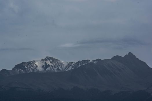 在乌云密布的阴沉天空下，白雪皑皑的山脉显得格外壮丽，构成一幅绝佳的冬日景致