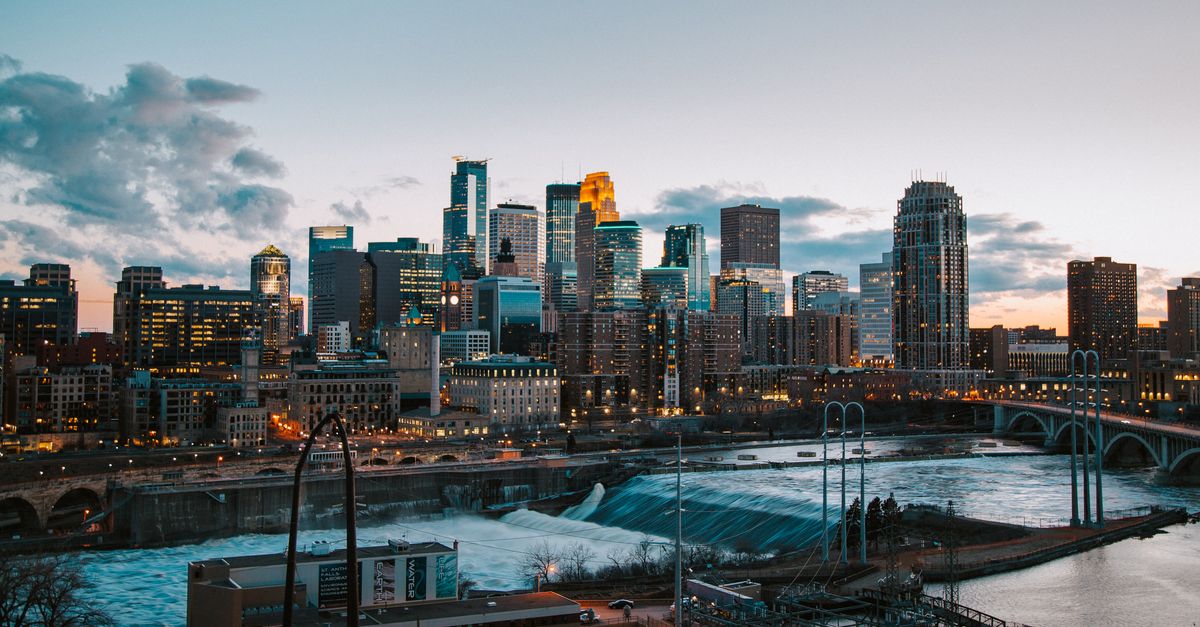 Stunning view of Minneapolis skyline with river and bridge at sunset.
