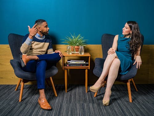 Free Woman Wearing Teal Dress Sitting on Chair Talking to Man Stock Photo